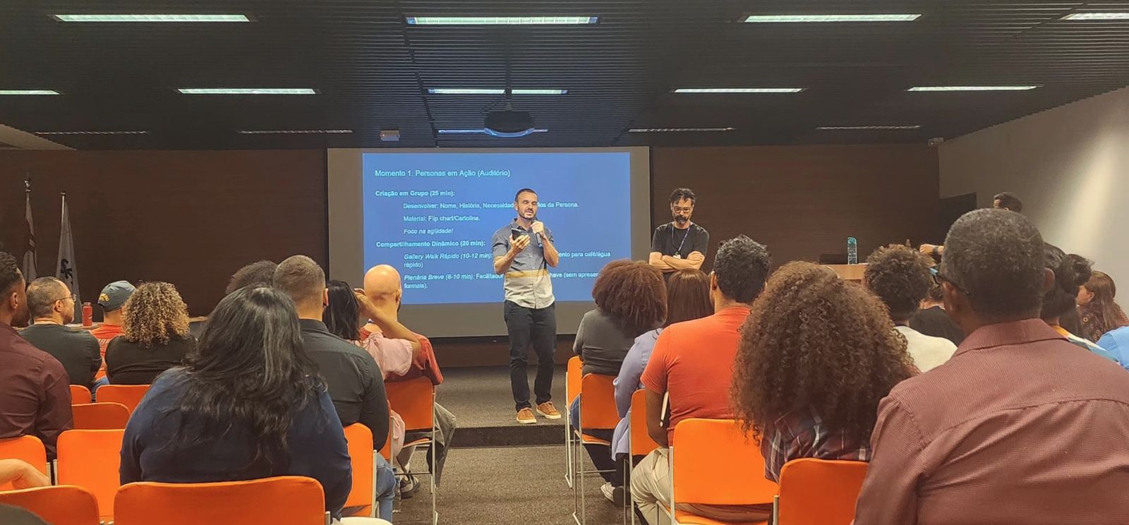 Alex Cói no palco, falando ao microfone para uma plateia durante a Oficina de IA do Senac.